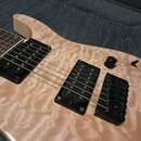 Detailní pohled na tělo elektrické kytary s přírodním povrchem z plamenového javoru. Nástroj je vybaven dvěma černými humbuckery a černým mostem. Na…