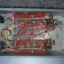 Fotografie zachycuje vnitřek šedého kovového šasi s elektronickým zapojením. Uprostřed je hnědá deska s viditelnými cestami a přilutovanými červenými…