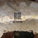 Detailní pohled na povrch mosazného činele. Uprostřed je černý nápis RIDE a pod ním označení 20"/51 cm. Povrch vykazuje známky opotřebení v podobě sk…