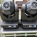 Dvě černé pohyblivé hlavice (moving heads) umístěné na černém transportním kufru s hliníkovým rámem. Na zadních panelech jsou vidět konektory XLR, na…