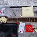Elektrická kytara krémové barvy s hnědým hmatníkem a světlou hlavou, na které je nápis Fender STRATOCASTER. V kufru se nachází černý koženěnýPouch s…