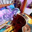Fotografie zachycuje hnědou akustickou kytaru z pohledu zezadu a zespodu. Na horní části korpusu jsou vidět dva ovládací knofíky. V pozadí jsou vidět…