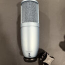 Stříbrný kondenzátorový mikrofon s mřížkou v horní části a matným povrchem těla. V dolní části je nápis DESIGNED IN AUSTRIA, pod ním MADE IN CHINA (P…