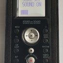 Černý přenosný digitální nahrávač značky KORG. Na displeji je text KORG SR1 SOUND ON a fialový sloupec indikátoru. Pod displejem je nápis SOUND on SO…