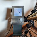 Elektronický modul v kovovém stříbrném provedení s displejem. Na displeji je nápis < STUDIO F > a v dolní části ikony s popisky Volume, Solo, Click,…
