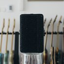 Černý efekt pedál s texturovaným povrchem. Na přední straně nejsou vidět žádné značky, loga ani nápisy. Za přístrojem jsou v pozadí rozostřené krky e…