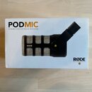 Fotografie znázorňuje bílé originální balení mikrofonu. Na krabici je nápis PODMIC a text DYNAMIC PODCASTING MICROPHONE, vpravo dole logo RØDE MICROP…