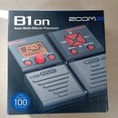 Fotografie znázorňuje krabici od efektového procesoru s nápisy B1on a Bass Multi-Effects Processor. V pravém horním rohu je logo ZOOM. Na obrázku pří…