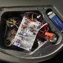 Fotografie zachycuje vnitřní elektroniku nástroje v šedém plastovém nebo lakovaném korpusu. Uprostřed je umístěna tiskovaná spoje s komponenty a nápi…