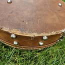 Detail hnědého koženého nebo syntetického pouzdra na hudební nástroj. Povrch je opotřebovaný a v horní hraně výrazně odřený s viditelným roztržením m…