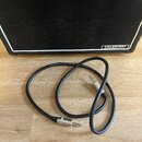 Černý audio kabel s konektory typu jack v kovovém provedení. Na kabelu je bílý nápis PROFESSIONAL LOW-NOISE 22 AWG SPEAKER. V pozadí je vidět část če…