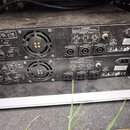 Zadní strana dvou černých rackových zesilovačů umístěných nad sebou. Na obou zařízeních jsou vidět stejné nápisy: „SUPPLY AC 220-240V~50Hz RATED INPU…
