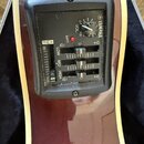 Detail na černý plastový předzesilovač s ovládacími prvky zabudovaný v těle kytary. Na panelu je nápis YAMAHA s logem, otočný knoflík VOL. a tři posu…