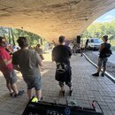 V popředí je digitální mixovací pult černé barvy s nápisy ALLEN&HEATH a Qu-24. Zařízení obsahuje několik řad knoflíků, posuvníků a barevný displej. V…