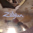 Detailní záběr na povrch mosazného činele. Uprostřed je bílý nápis Zildjian. Povrch vykazuje známky opotřebení v podobě zahlreichen škrábanců a zneči…