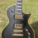 Černá elektrická kytara s gold-hardwarem a žlutým lemováním kolem korpusu. Nástroj má dva humbuckery, Tune-o-matic kobylku a tři otočné knofíky. Hmat…