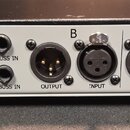 Zadní panel bílého elektronického zařízení s černým šasi. Na levé straně jsou nápisy 5043, DUO COMP, POWER, LINK, A BUSS IN a B BUSS IN u příslušných…