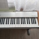 Digitální piano stříbrné barvy s dřevěnými bočními panely. Na pravé straně korpusu je nápis DIGITAL PIANO PS-20. V levé části jsou ovládací tlačítka…
