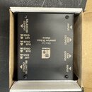 Černá DI box v kartonové krabici. Na zařízení je bílý nápis „Palmer“, logo s palmou a text „PAN 04 passive DI box stereo“. Jsou zde označení vstupů a…
