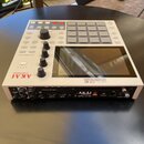 Bílá MPC sampler s šedými pady, ovládacími knoflíky a displejem. Na přední straně je červené logo AKAI professional a nápis MPC ONE MUSIC PRODUCTION…