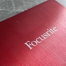 Detailní záběr na červený kovový povrch s jemným broušením. Uprostřed je bílý nápis Focusrite. Povrch vykazuje drobné nečistoty a škrábance.