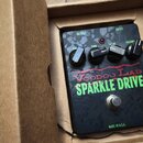 Kytarový efekt pedál v kartonové krabici. Na černém povrchu s texturou jsou nápisy Voodoo Lab a SPARKLE DRIVE, v dolní části je text MADE IN U.S.A. P…