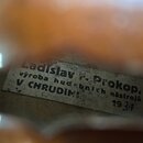 Detailní pohled na papírový štítek uvnitř hudebního nástroje. Na štítku je černý text: „Ladislav F. Prokop, výroba hudebních nástrojů V CHRUDIMI 1931…