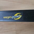 Detail černého kovového profilu s nalepenou nálepkou. Na nálepce je žlutý grafický symbol a modrý nápis soundsation. Povrch profilu vykazuje drobné p…