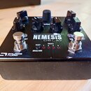 Černý efekt pedál s kovovým povrchem. Na horní straně je nápis NEMESIS DELAY a v levém dolním rohu logo SOURCE AUDIO. Zařízení má čtyři černé ovládac…