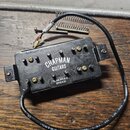 Černý elektrický snímač s kovovými póly a připojovacím kabelem. Na povrchu je bílý nápis CHAPMAN GUITARS a malá nálepka s textem SONOROUS BRIDGE. Na…