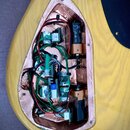 Fotografie zachycuje otevřenou elektronickou výrubku v těle žluté kytary. Vnitřní prostor je vyložen měděnou stínící páskou a obsahuje rozvedení bare…