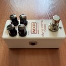 Bílý efekt pedál s čtyřmi černými oválnými knoflíky. Na horní straně jsou nápisy SENSITIVITY, TONE, CLEAN a OUTPUT, logo MXR v červeném rámečku a tex…