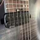 Detail elektrické kytary s hmatníkem z tmavého dřeva a šedým lakovaným tělem. Na těle jsou dva černí humbuckery, z nichž na spodním je bílý nápis EMG…