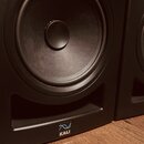 Černý studiový monitor s viditelným nízkofrekvenčním reproduktorem. V dolní části je umístěno logo znázorněné dvěma vlnovkami a nápis KALI. Povrch je…