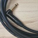 Černý instrumentální kabel s úhlovým zlatým konektorem. Na povrchu kabelu je bílý nápis GUITAR 1x0,75 MM² CGK 175 GERMANY. Kabel i konektor vykazují…