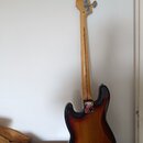 Zadní pohled na elektrickou basovou kytaru s trupem v barevném přechodu od žluté přes hnědou k černé. Na hlavě nástroje je vidět logo "Fender" a nápi…