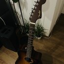 Akustická kytara s cutawayem v tmavě hnědé barvě s přechodem do světlejší žluté v centru korpusu. Na hlavě hmatníku je zlatým písmem nápis Fender. Na…