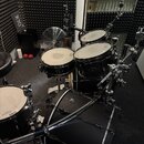 Černá bicí souprava s kovovým hardwarem. Na basovém bubně je viditelné logo značky Mapex a na stojanu nápis Gibraltar. Souprava obsahuje basový buben…