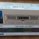 Na fotografii jsou dvě krabice s hudební technikou. Horní bílá krabice nese nápisy GX Series GX5, logo QSC a webovou adresu www.qscaudio.com. Spodní…