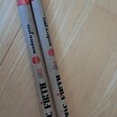 Dvě bubenícké paličky z dřeva s červeným gripem v horní části a modrými špičkami. Na obou jsou čitelné nápisy „modern jazz“, logo „VIC FIRTH“ a označ…