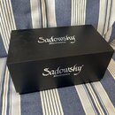 Černý obdélníkový box s matným povrchem. Na horní i přední straně je bílý nápis „Sadowsky Electronics“. Povrch vykazuje lehké znečištění v podobě pra…