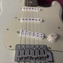 Bílá elektrická kytara s bílým pickguardem a třemi bílými snímači. Na spodním snímači je nápis Seymour Duncan. Kytara má chromovaný kobylník a jeden…