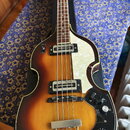 Elektrická basová kytara s polodupatým korpusem v barevném přechodu od žluté přes oranžovou k hnědé. Nástroj má bílý perleťový pickguard a černý ovlá…