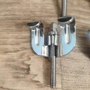 Fotografie zachycuje dva kovové ladicí mechanismy v chromovém provedení položené na dřevěném povrchu. Jsou vidět závitové šrouby a držáky strun. Na s…