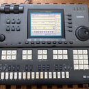 Šedý music sequencer značky YAMAHA, model QY700. Zařízení má v horní části displej s modrým podsvícením a pod ním řadu ovládacích tlačítek. V pravé č…