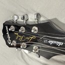 Fotografie zachycuje hlavu černé elektrické kytary s chromovanými ladičkami. Na hlavě jsou bílé nápisy Epiphone, Les Paul a Studio LT, dále je zde me…
