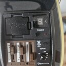 Detailní pohled na černý elektronický preamp s vestavěným ladičkou. Na plastovém krytu je vyražené logo Takamine a pod displejem ladičky je nápis TUN…