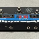 Černý efekt pedál s nápisy Radial, JX-2 a ToneBone. Na horní straně jsou dva stomečové spínače s popisky BOOST a BOTH, centrální zapínací tlačítko s…