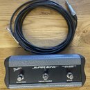 Fotografie zobrazuje černý kabel s konektory a ovládací pedál v stříbrno-černém provedení. Na pedálu je bílé logo Fender's a nápis SUPER-SONIC™. V pr…