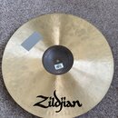 Zlatavý kovový činel s viditelnou strukturou kování. Na povrchu je černý nápis Zildjian a v horní levé části se nachází šedý obdélníkový štítek. V ce…
